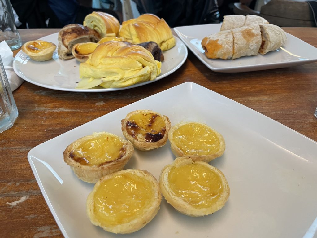 Two trays of breakfast sandwiches and pastais de natas, a Portuguese custard tart